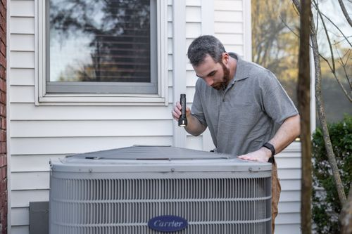 HVAC technician inspecting a residential Carrier air conditioner condenser unit outside a Kansas City home
